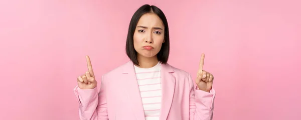 伤心的亚洲女商人，专业的公司经理指指点点，闷闷不乐，站在粉红的背景上 — 图库照片