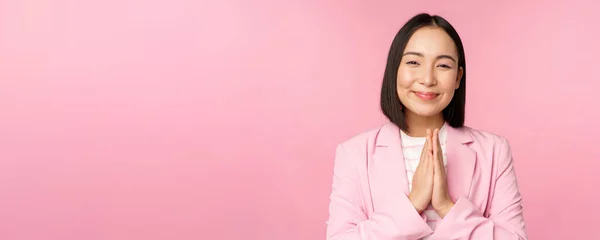 Да, спасибо. Улыбающаяся азиатская продавщица, корпоративная леди в костюме благодарная, держащаяся за руки в сумке, жест благодарности, стоящая на розовом фоне — стоковое фото