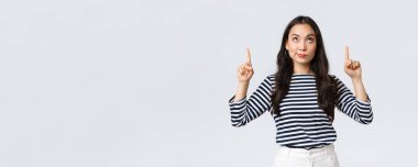 Yaşam tarzı, güzellik ve moda, insanların duygu konsepti. Kararsız ve kuşkulu Asyalı bir kadın garip bir reklamı işaret ediyor, kuşkuları var, satın almadan önce tereddüt ediyor.