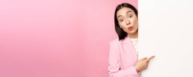 Genç Japon iş kadınının portresi, takım elbiseli kurumsal bayan duvarda çizelgeyle işaret ediyor, boş fotokopi alanı üzerinde diyagram veya reklam gösteriyor, pembe arka plan