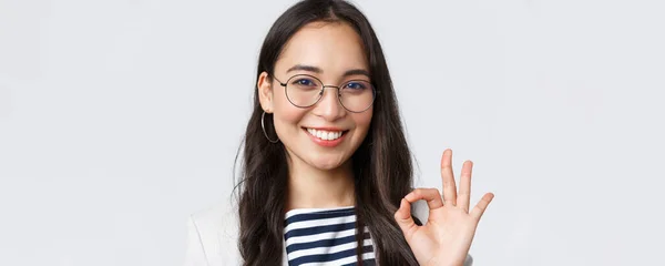 Negocios, finanzas y empleo, concepto de emprendedoras exitosas. Primer plano de alegre oficina dama, asiático secretario de banco en gafas, sonriendo y mostrando buen gesto en la aprobación — Foto de Stock