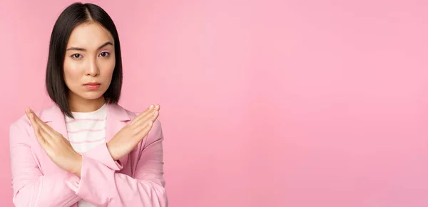 Εικόνα της σοβαρής εταιρικής γυναίκας, ασιάτισσα επιχειρηματίας δείχνει στάση, σταυρό χειρονομία, αποδοκιμάζει smth, στέκεται στο κοστούμι πάνω από ροζ φόντο — Φωτογραφία Αρχείου