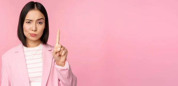 Azjatycka bizneswoman z poważnym, zaniepokojony wyraz twarzy, pokazując zatrzymanie ruchu, tabu, zakazać gestu, dezaprobata smth źle, stojąc nad różowym tle — Zdjęcie stockowe