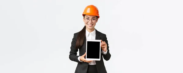 직업 여성 기술자, 판매원 또는 부동산 중개업자가 고객에게 위치를 보여 주고, 안전 헬멧과 비지니스 슈트를 착용하고 태블릿 화면에서 건설 프로젝트를 소개 한다. — 스톡 사진