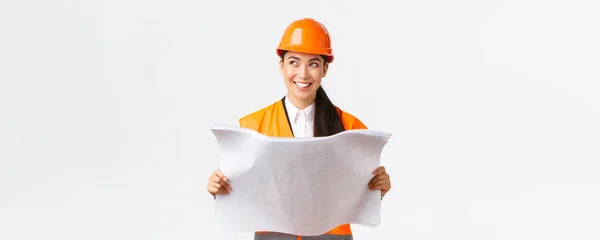 Créatif asiatique femme architecte imagerie son plan, debout dans la sécurité casque et regarder loin réfléchi tout en lisant les plans, image buiding après finition travaux de construction, fond blanc — Photo