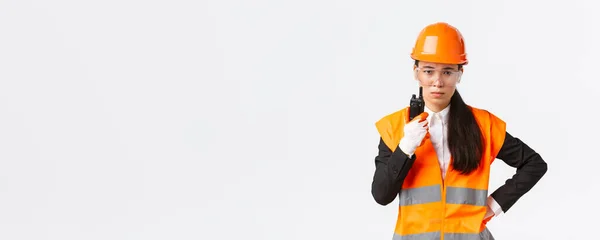 Desapontado asiático feminino engenheiro de construção, técnico ou gerente industrial em uniforme de segurança chamando empregado via walkie-talkie, repreendendo pessoal usando comunicação de rádio na empresa — Fotografia de Stock