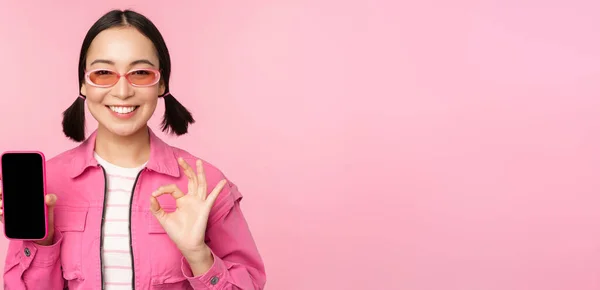 Entusiasta giovane donna asiatica mostrando ok, ok segno, sorridente soddisfatto, schermo del telefono cellulare, applicazione smartphone, in piedi su sfondo rosa — Foto Stock