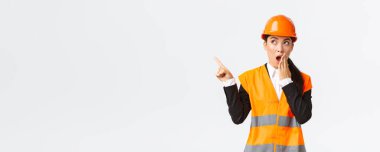 Şaşırmış ve etkilenmiş Asyalı kadın mühendis, güvenlik kaskı ve yansıtıcı ceketli inşaat müdürü, sol üst köşesinde nefes nefese kalmış parmak, hayrete düşmüş, ilginç bir şey buldu.