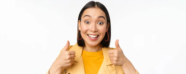 Sorrindo asiático menina mostrando polegares para cima, olhando satisfeito, aprovar smth, de pé sobre branco fundo — Fotografia de Stock