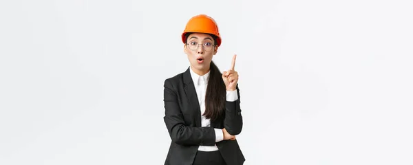 Креативная умная женщина - инженер-строитель имеет отличную идею, стоит в защитном шлеме, костюме, поднимает указательный палец, говорит мысль или предложение, находит решение, делится своим планом, белым фоном — стоковое фото