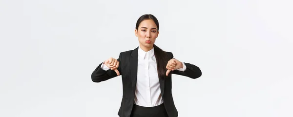Oroad skeptisk kvinnlig kontorschef, säljare i svart kostym visar tummen ner och grimma som beskriver något lam och hemskt, klagar på dålig kvalitet, vit bakgrund — Stockfoto