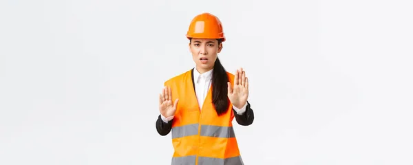 Csalódott dühös ázsiai női mérnök biztonsági sisak és fényvisszaverő ruházat mondván stop, tiltani és nem ért egyet az építési vezető, mutatja elég, nincs gesztus, fehér háttér — Stock Fotó