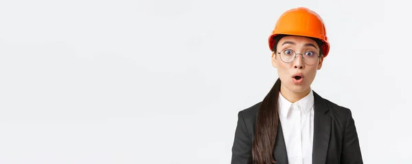 Close-up van geschokte en bezorgde Aziatische vrouwelijke ingenieur horen slecht nieuws, verontrustende aankondiging, staan in veiligheidsmasker, bril en business suit en hijgend geschrokken, witte achtergrond — Stockfoto