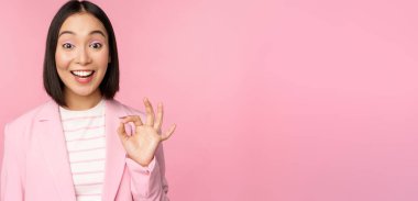 - Çok iyi. Mutlu Koreli iş kadını gülümsüyor. Memnun, tamam işareti gösteriyor, aferin, mükemmel bir seçim jesti. Pembe arka planda duran Slamth 'a şükret.