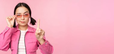 Ciddi yüzlü Asyalı bir kız resmi, yasaklama, azarlama hareketi, parmağını sallama, onaylamadığını ifade etme, pembe arka planda durma