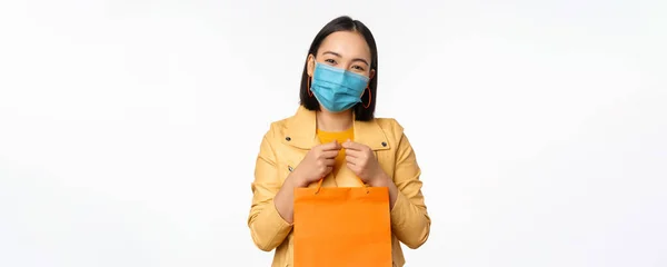 Covid-19 és üzletkoncepció. Fiatal ázsiai stílusos nő, orvosi maszkot visel, kezében bevásárló táska, megy a plázákban világjárvány idején, fehér háttér — Stock Fotó