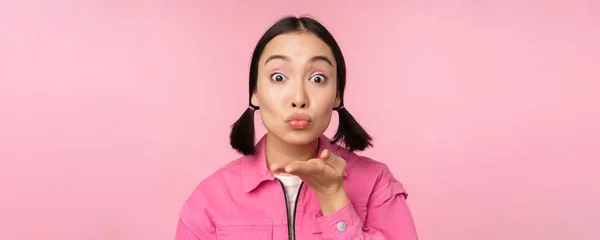 Close up retrato de bela menina asiática boba, enviando beijo de ar, mwah na câmera, soprando, de pé sobre fundo rosa — Fotografia de Stock