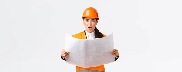 Frustrée et mécontente femme ingénieur asiatique, architecte en chef de la zone de construction, à la recherche déçue après avoir étudié les plans, caméra de regard, gestionnaire de grondement, fond blanc — Photo