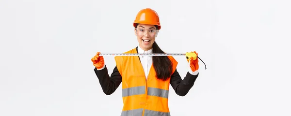 Excité et optimiste asiatique femme ingénieur de construction mesure disposition, tenant mètre ruban et sourire, prêt pour le travail à construire quelque chose, debout sur fond blanc dans le casque de sécurité — Photo