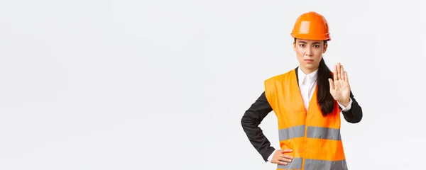 Serious-olhando decepcionado asiático arquiteto feminino, gerente de construção na área de trabalho vestindo capacete de segurança, mostrando stop gesto, proibir a ação, proibir a invasão, fundo branco — Fotografia de Stock