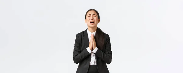 Overwerkte en verdrietige Aziatische zakenvrouw smekend om hulp, schreeuwende hand in hand, smekend en huilend wanhopig, staande van streek over witte achtergrond — Stockfoto