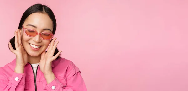 Κοντινό πλάνο της κομψής Κορεάτισσας με γυαλιά ηλίου, χαμογελώντας χαρούμενη, ποζάροντας σε ροζ φόντο. Οι άνθρωποι αντιμετωπίζουν την ιδέα — Φωτογραφία Αρχείου