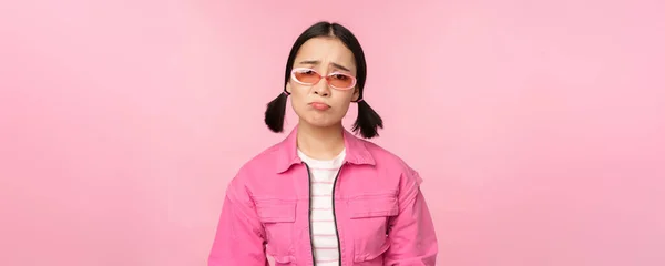 Porträt eines traurigen und düsteren asiatischen Mädchens, das vor Enttäuschung schmollt und aufgebracht vor rosa Studiohintergrund steht — Stockfoto