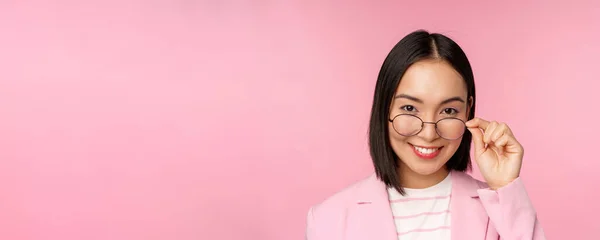 안경을 쓴 동양 여성 이 카메라에 흥미를 느끼고 웃는 모습, 섹시 한 점원 이 관심을 가지고 분홍색 배경을 응시하는 모습 — 스톡 사진