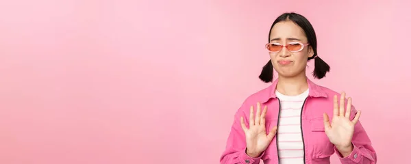 Ні, дякую. Зіпсована азіатська дівчина в сонцезахисних окулярах, відкидаючи smth, трясучи руки, щоб відмовитися, відмовитися, стоячи на рожевому фоні — стокове фото