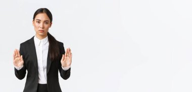 Ciddi görünümlü hoşnutsuz Asyalı kadın yönetici, siyah takım elbiseli iş kadını bir şeyi yasaklayan ya da yasaklayan, yasaklayan el kaldıran, hayır ya da yeterince beyaz arka plan diyen,