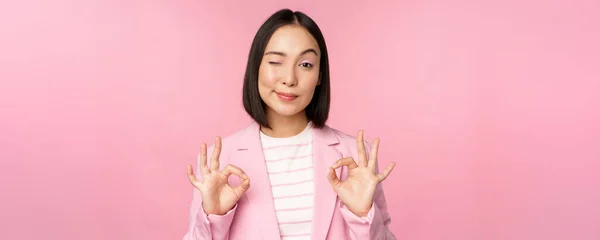 Okay, excellent. Businesswoman in corporate suit, showing ok, approval gesture, recommending smth, give positive feedback and smiling pleased, posing over pink background — Stock Photo, Image
