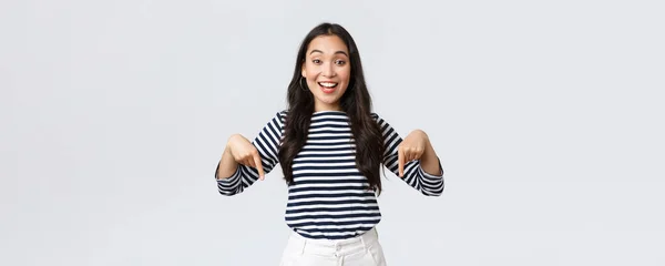 Estilo de vida, belleza y moda, concepto de emociones de la gente. Emocionado tierna chica asiática encantadora con linda sonrisa señalando los dedos hacia abajo, invitando a los clientes a un evento especial, fondo blanco — Foto de Stock