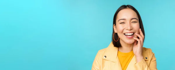 Крупным планом портрет естественной азиатской девушки смеющейся, улыбающейся и выглядящей счастливой, стоящей на синем фоне — стоковое фото
