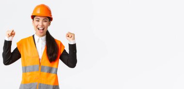 Başarılı bir şekilde Asyalı kadın mühendis yumruk pompası kazandı ve evet diye bağırdı evet memnun, güvenlik kaskı ve ceket giydi, zafere karşı zafer kazandı, inşaatı zamanında bitirdi, beyaz arka planda durdu.