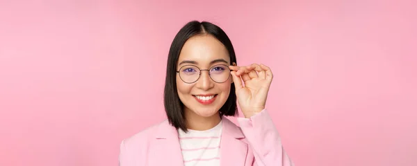 Primer plano retrato de mujer corporativa asiática, mujer de negocios profesional en gafas, sonriendo y mirando con confianza a la cámara, fondo rosa — Foto de Stock