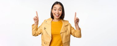 Hevesli Asyalı kız parmaklarını havaya kaldırıyor, üstte reklamını gösteriyor, mutlu bir şekilde gülümsüyor, tanıtım teklifi ya da afiş sunuyor, beyaz arka planda duruyor.