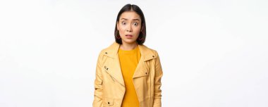 Şok olmuş, kafası karışmış Asyalı bir kadının görüntüsü. Hayal kırıklığına uğramış ve nutku tutulmuş bir şekilde kameraya bakıyor, kaşlarını kaldırıyor ve endişeli bir şekilde beyaz arka planda duruyor.