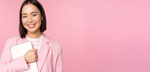 Εικόνα της νεαρής Κορεάτισσας εταιρικής γυναίκας, CEO manager κρατώντας ψηφιακή ταμπλέτα, χαμογελώντας και δείχνοντας επαγγελματίας, φορώντας κοστούμι, στέκεται πάνω από ροζ φόντο — Φωτογραφία Αρχείου