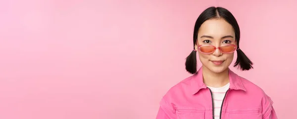 Close-up van stijlvolle Koreaanse meisje in een zonnebril, glimlachend gelukkig, poseren tegen een roze achtergrond. Mensen worden geconfronteerd met concept — Stockfoto