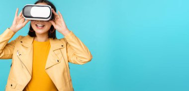 VR kulaklık takan mutlu Asyalı kadın modelin portresi. Sanal gerçeklik gözlükleriyle gülüyor ve gülümsüyor. Mavi arka planda duruyor.