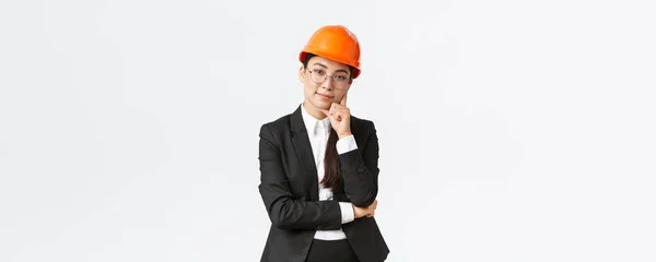 Mosolygó professzionális ázsiai üzletasszony befektetni pénzt az építőiparban, kezelni a munkát a vállalkozás, visel biztonsági sisak és öltöny, látszó elégedett kamera, álló fehér háttér — Stock Fotó
