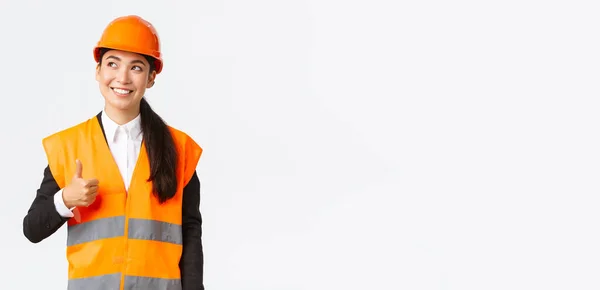 행복 한 미소짓기 여성 아시아인 건축가, 안전 헬멧과 반사 재킷을 입고 서서 왼쪽 위를 보며 승인의 엄지손가락을 보여 주는 건설 작업에 만족 — 스톡 사진