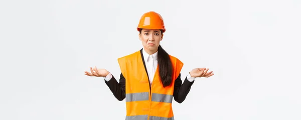 Upset and confused asian female engineer feeling complicated, raising hands sideways and shrugging, dont know why, have no idea, being clueless, pouting and being sad, white background — Stock Photo, Image