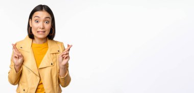 Heyecanlı Asyalı kadın portresi umut dolu, dua eden, yalvaran, haber bekleyen, beyaz arka planda duran, mutlu gülümseyen,