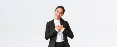 Gülümseyen mutlu Asyalı bayan girişimci övgü ya da iltifat alır, kalbe el ele tutuşur, sırıtır, pohpohlanır, minnettar hisseder, beyaz arka planda durur.