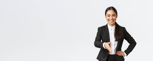 Confident smiling asian businesswoman extend hand for firm handshake, greeting client or business partner to sign deal, looking determined and ready, standing white background