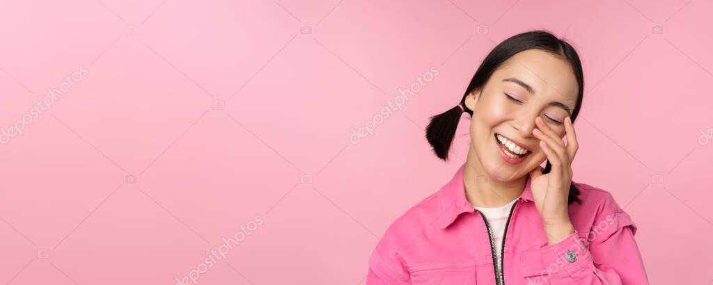 Close up portrait of beautiful asian girl looking enthusiastic and smiling, laughing and smiling, standing happy against pink background.
