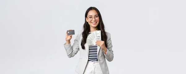Wirtschaft, Finanzen und Beschäftigung, Unternehmer und Geldkonzept. Erfolgreiche asiatische Geschäftsfrau zeigt, wie Einkommen erhöhen, halten Kreditkarte und Geld, lächelnde Kamera — Stockfoto