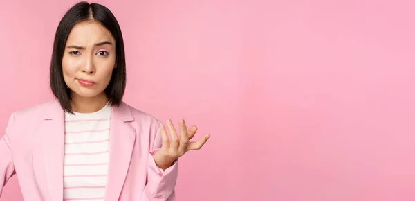 Portrait de femme asiatique en colère en costume, les poings serrés et l'air furieux, indigné de smth mauvais, debout sur fond rose — Photo