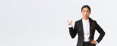 Şüpheci ve garip Asyalı genç iş kadını, siyah takım elbiseli satış elemanı küçük bir şeyi şekillendiriyor ve boyut olarak hayal kırıklığına uğramış görünüyor, ufak tefek şeylerle eğlenmiyor, beyaz arka plan.